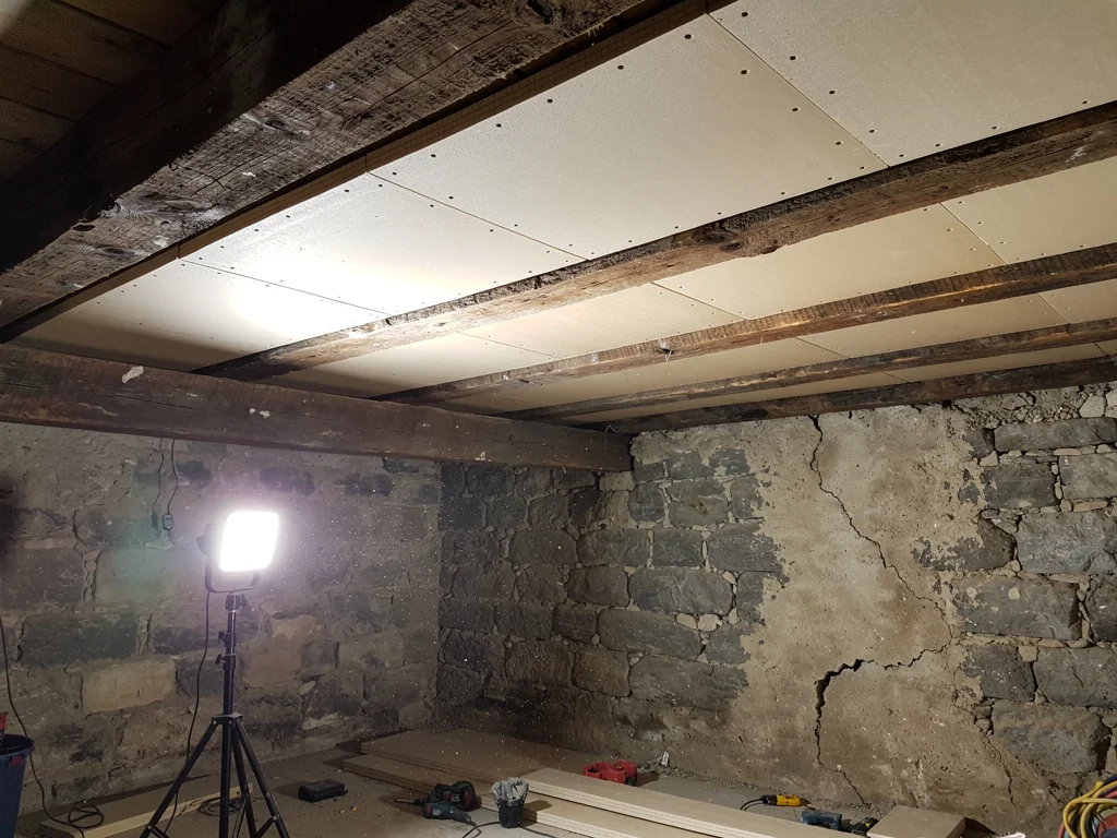 Plafond de cave voûtée isolé par panneaux sous le plancher ancien